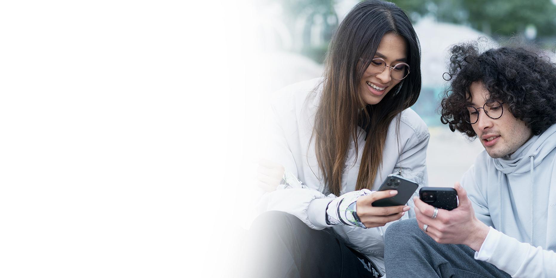 Two young people, a woman with long brown hair smiling and a boy with curly black hairs wearing ZEISS SmartLife glasses looking at their phones. 