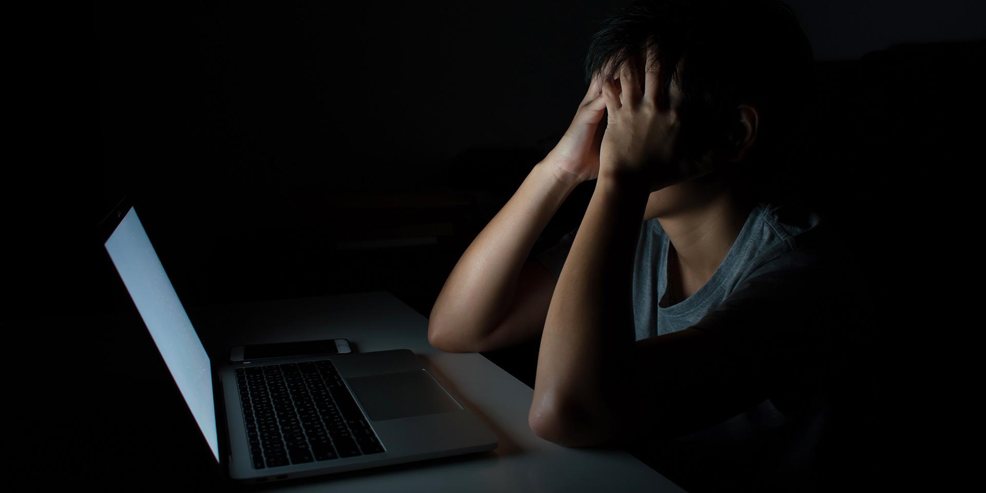 A young man in front of a laptop with high brightness in a poorly lighted room.