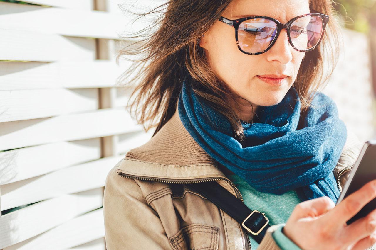 Woman holding takeaway coffee and using smart phone