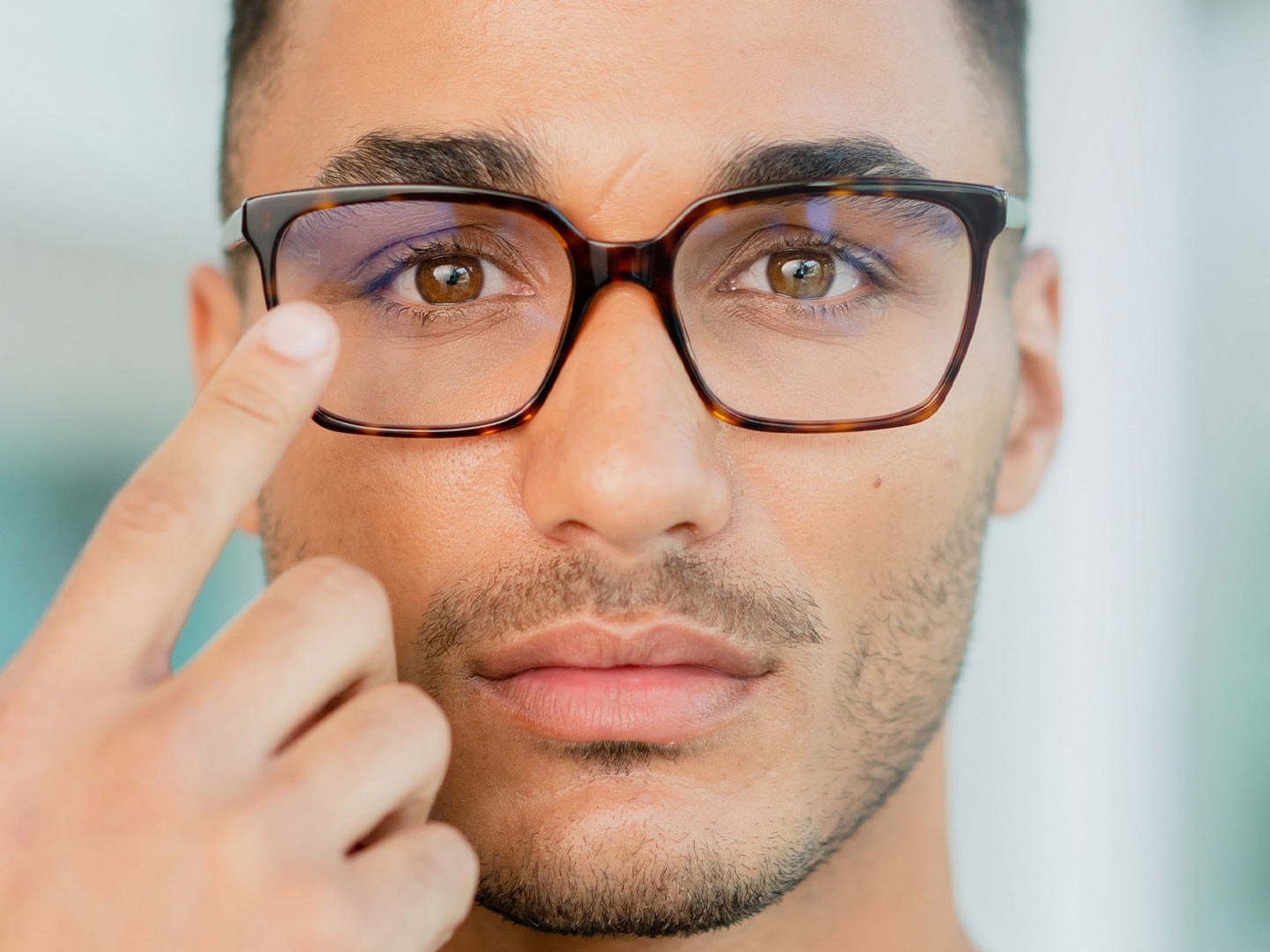 A man with glasses touching the surface of his glasses